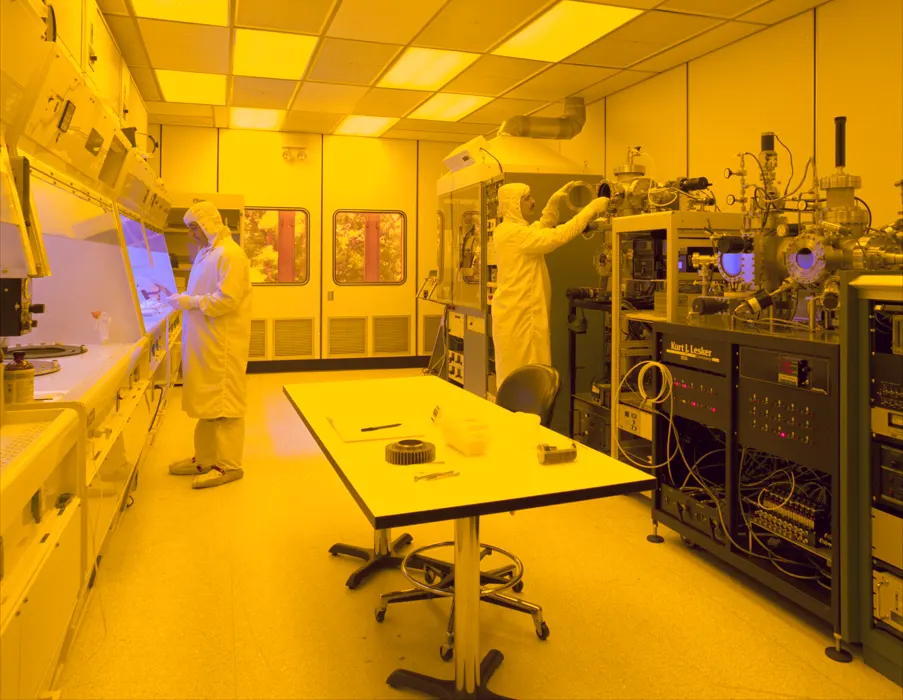 Two technicians work at equipment in a semiconductor cleanroom.